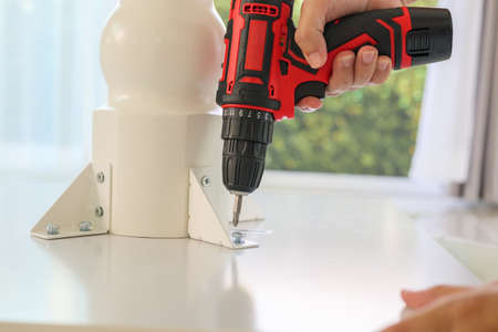 man assembling white table furniture at home using cordless screwdriver