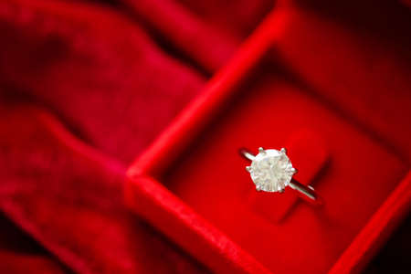 Diamond ring in jewelry gift box on red fabric backgroundの写真素材