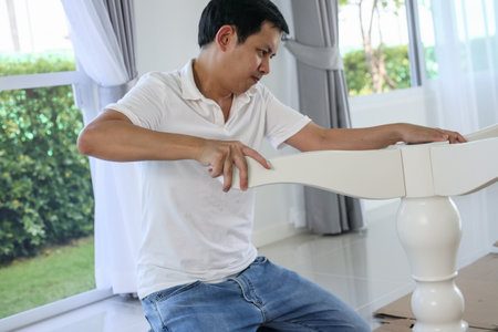Asian man assembling white table furniture at homeの写真素材