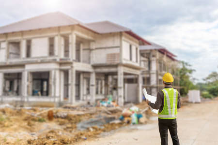 young professional engineer in protective helmet and blueprints paper at the house building construction siteの写真素材