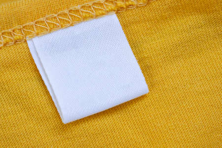 White blank clothing tag label on new yellow shirt background