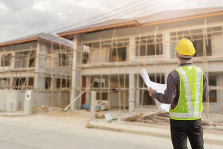young professional engineer in protective helmet and blueprints paper at the house building...