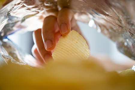 Hand picking potato chips inside snack bag