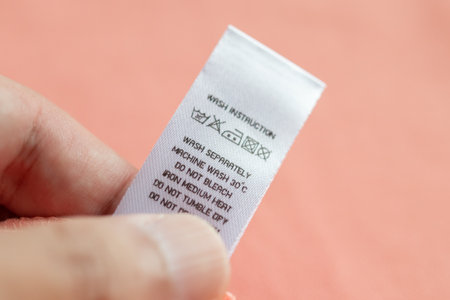 Hand hold and reading at white laundry care washing instructions clothes label on pink shirtの写真素材