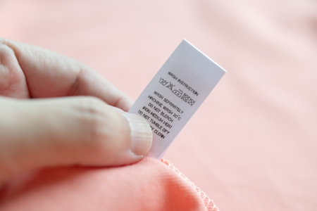 Hand hold and reading at white laundry care washing instructions clothes label on pink shirt