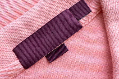 Blank red laundry care clothes label on pink fabric texture background