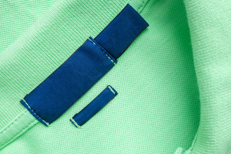 Blank blue laundry care clothes label on green shirt fabric texture background
