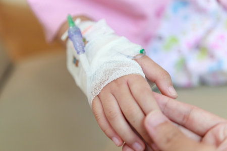 Mother holding child hand with saline IV solution in hospitalの写真素材