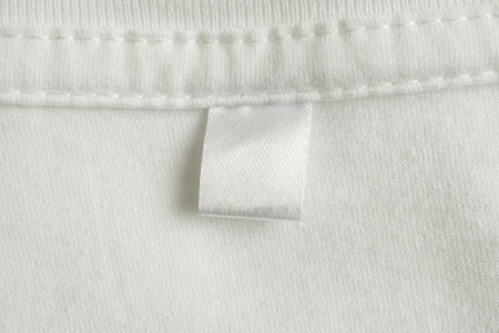 Blank white laundry care clothes label on white shirt fabric texture background