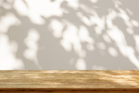 Empty wood table top on beige wall texture with tree leaves shadow backgroundの写真素材