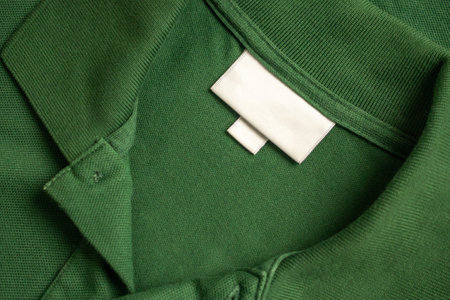 Blank white laundry care clothes label on green shirt fabric texture background