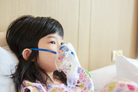 Sick little asian girl inhalation with nebulizer for respiratory treatmentの写真素材