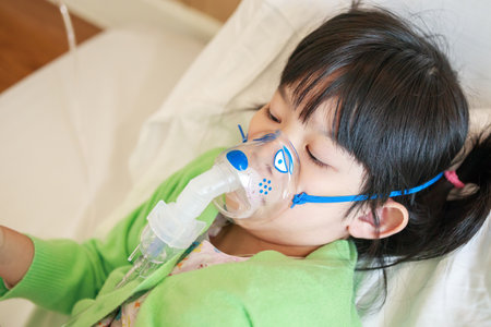Sick little asian girl inhalation with nebulizer for respiratory treatmentの写真素材