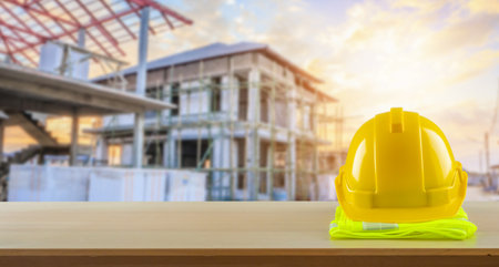 Yellow safety construction helmet on wood table with construction site backgroundの写真素材