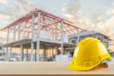 Yellow safety construction helmet on wood table with construction site backgroundの写真素材