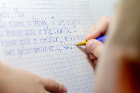 Close-up of boy hand with pencil writing english words by hand on traditional white notepad paper....