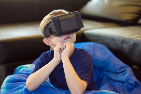 Happy teen boy wearing virtual reality goggles watching movies or playing video games. Cheerful...