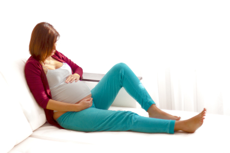 Pregnant caucasian woman relaxing at home on the white couchの写真素材