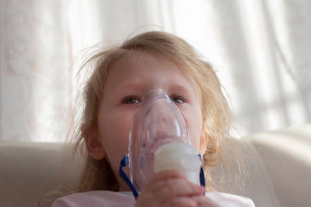 Little girl having inhalation for easing cough. Caucasian blonde girl inhales couples containing medication to stop coughing.の写真素材