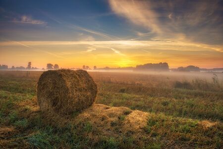 Beautiful summer sunrise over fields with hay balesの写真素材