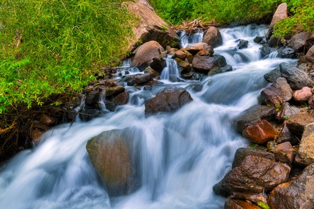Mountain Waterfall - blue water and huge boulders surrounded by green treesの写真素材
