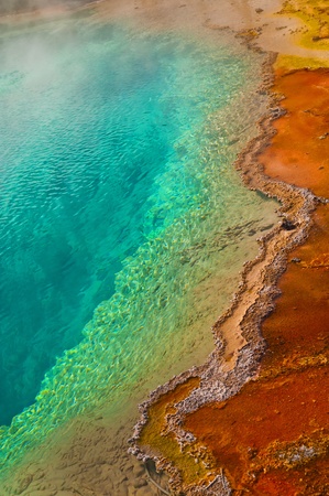 Beautiful cerulean geyser surrounded by colorful layers of bacteria, against cloudy blue sky の写真素材