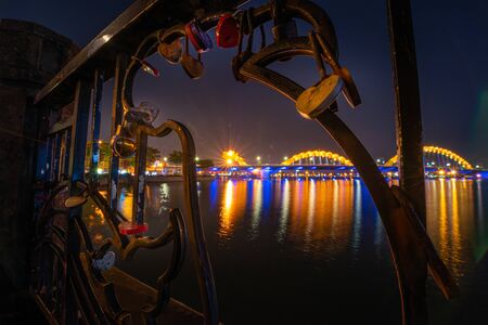 Close up of locked padlocks are placed on the Love Bridge as symbol of love. Nigtht view of the Dragon Bridge over the Han River in Da Nang, Vietnamの写真素材
