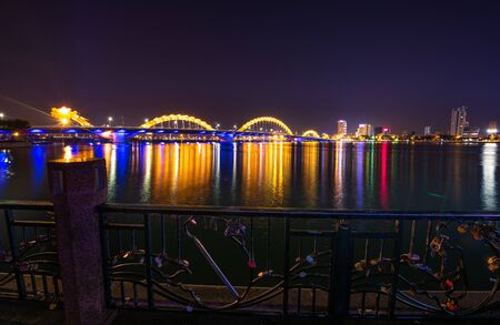 Locked padlocks  placed on the bridge as symbol of love. Dragon Bridge as seen from the Love Bridge in Da Nang, Vietnam.の写真素材