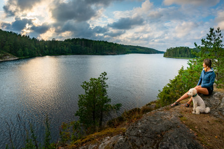 Young Woman with her dog admires beautiful Vansjo Lake Norwayの写真素材
