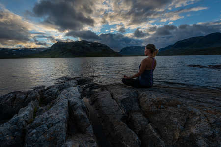 Woman practices yoga on the rocky shore of Stavatn Lakeの写真素材