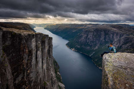 Backpacker sits on top of the Eagle Head Viewpoint near Kjeragboltenの写真素材