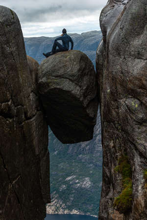 Tourist sits on top of Kjeragbolten - boulder wedged in the mountain's crevasse 984 meter above the seaの写真素材