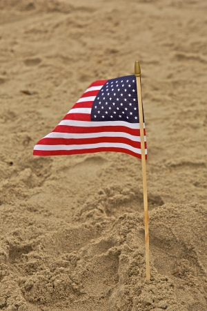A small American flag is planted into the sand at a beachの写真素材