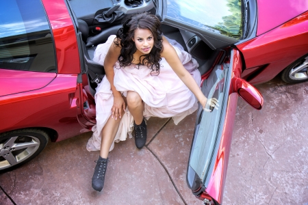 Glamorous young African American woman wearing a bustier and full length puffy pink skirt looks upward while getting out of the passenger seat of a sports car with the top removedの写真素材