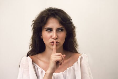 Close up photo portrait of young beautiful woman with freckles which shows quieter. Funny face on gray background. Don't tell anyone my secretの写真素材
