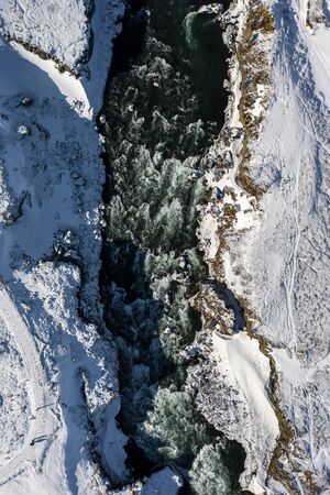 Aerial view of Godafoss waterfall, snowy shore and river. Iceland in early spring.