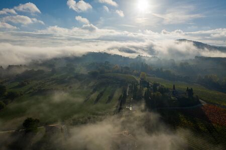 Aerial view of a rural landscape during sunrise in Tuscany. Rural farm, vineyards, green fields, sunlight and fog. Italy, Europe.の写真素材