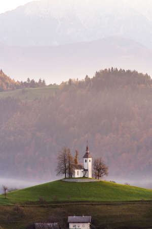 Skofja Loka, Slovenia - view of the beautiful Church of St. Tomaz (St. Thomas) on top of the hill with an amazing misty sunrise and the Julian Alps in the background in the fall.の写真素材