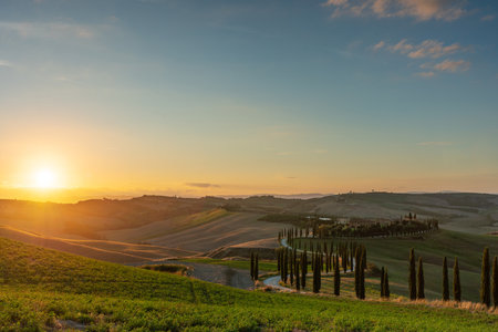 A wellknown Tuscan landscape with grain fields, cypresses and houses in the hills at sunset. Autumn rural landscape with winding road in Tuscany, Italy, Europe.の写真素材