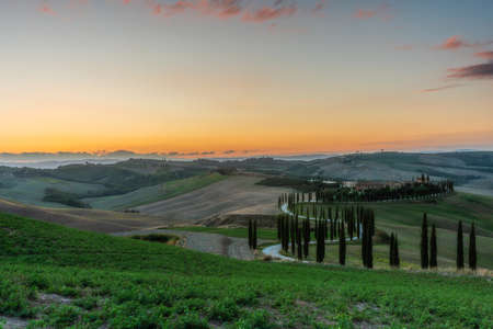 Tuscany, rural landscape at sunset. Rural farm, cypresses, green field, sunshine and clouds. Italy, Europe.の写真素材