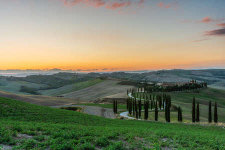 Tuscany, rural landscape at sunset. Rural farm, cypresses, green field, sunshine and clouds. Italy, Europe.の写真素材