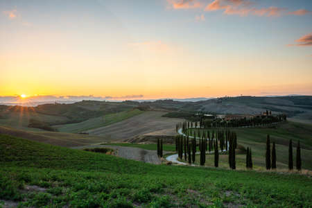 Tuscany, rural landscape at sunset. Rural farm, cypresses, green field, sunshine and clouds. Italy, Europe.の写真素材