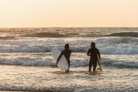 Surfers Heading into the Waves at Sunset in Peniche, Portugalの写真素材