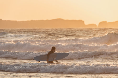 Surfer Walking in Waves at Sunset in Peniche, Portugalの写真素材