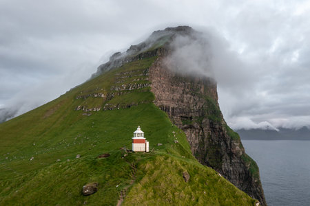 Stunning Coastal Lighthouse on Faroe Islands with Dramatic Mountain Backdropの写真素材