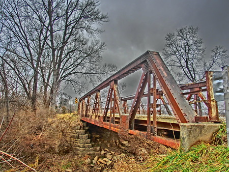 Old rusting bridge crossing a small stream with the rock supports beneath it falling.の写真素材