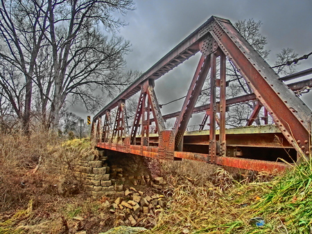 Old rusting bridge crossing a small stream with the rock supports beneath it falling.の写真素材