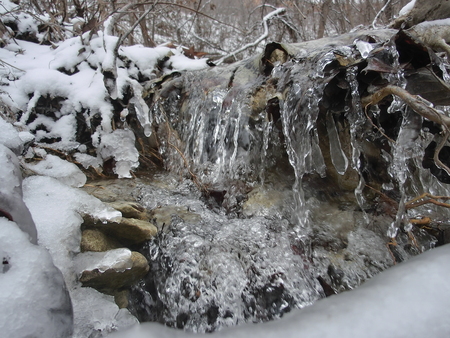Half frozen waterfall flowing over the edge of a small rock waterfall in a small creek with snow covering the side.の写真素材