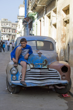 Teenager sitting on a broken down old classic car in Havana, Cubaのeditorial素材