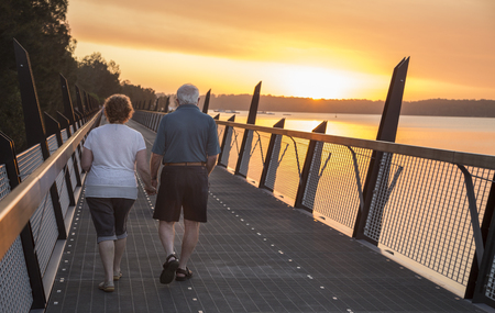 Retired Couple walking along walkway at sunsetの写真素材